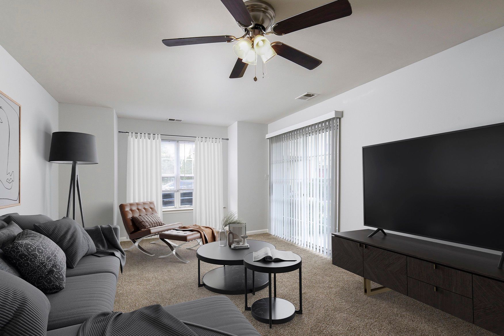 Living room in an apartment with gray sofa, coffee tables, large TV, ceiling fan, and vertical blinds.