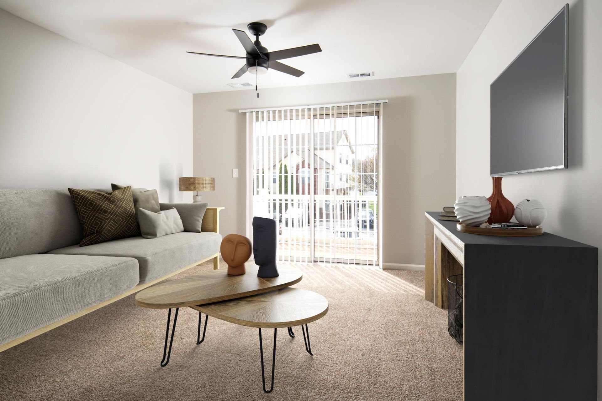 Bright apartment living room with gray sofa, coffee tables, TV on the wall, and sliding glass door to balcony.