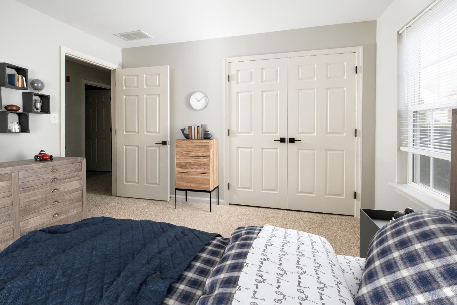 Bedroom in a modern apartment with a bed, dresser, double closet doors, and a window.