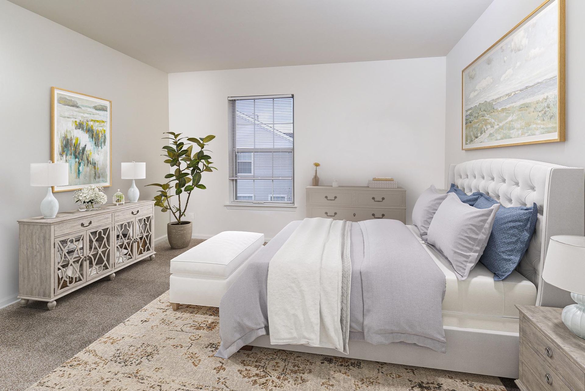 Furnished bedroom in a modern apartment with a white tufted bed, dressers, and a plant.