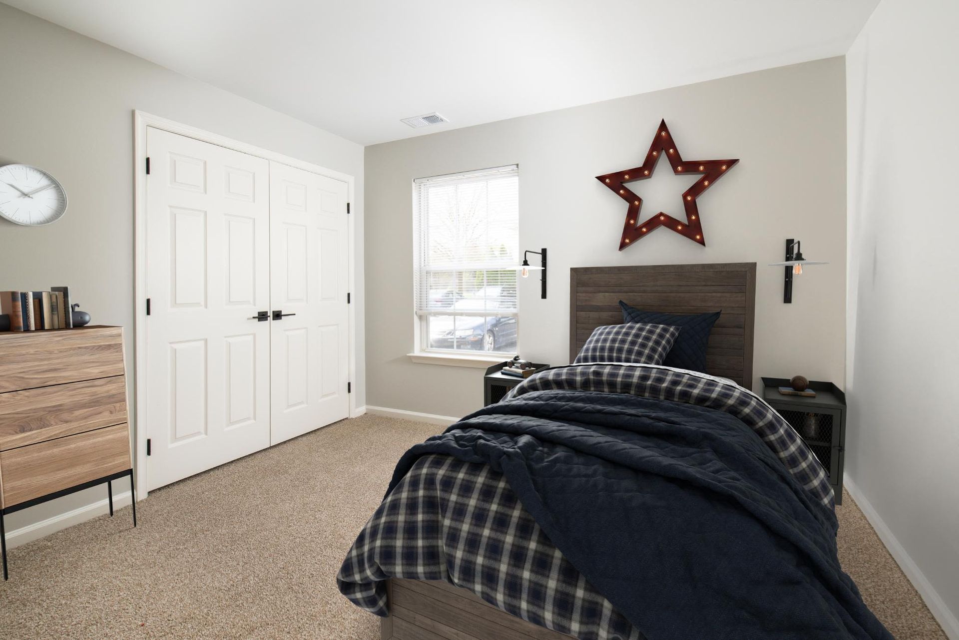 Bedroom with a wooden bed, plaid bedding, two nightstands, and star wall decor.