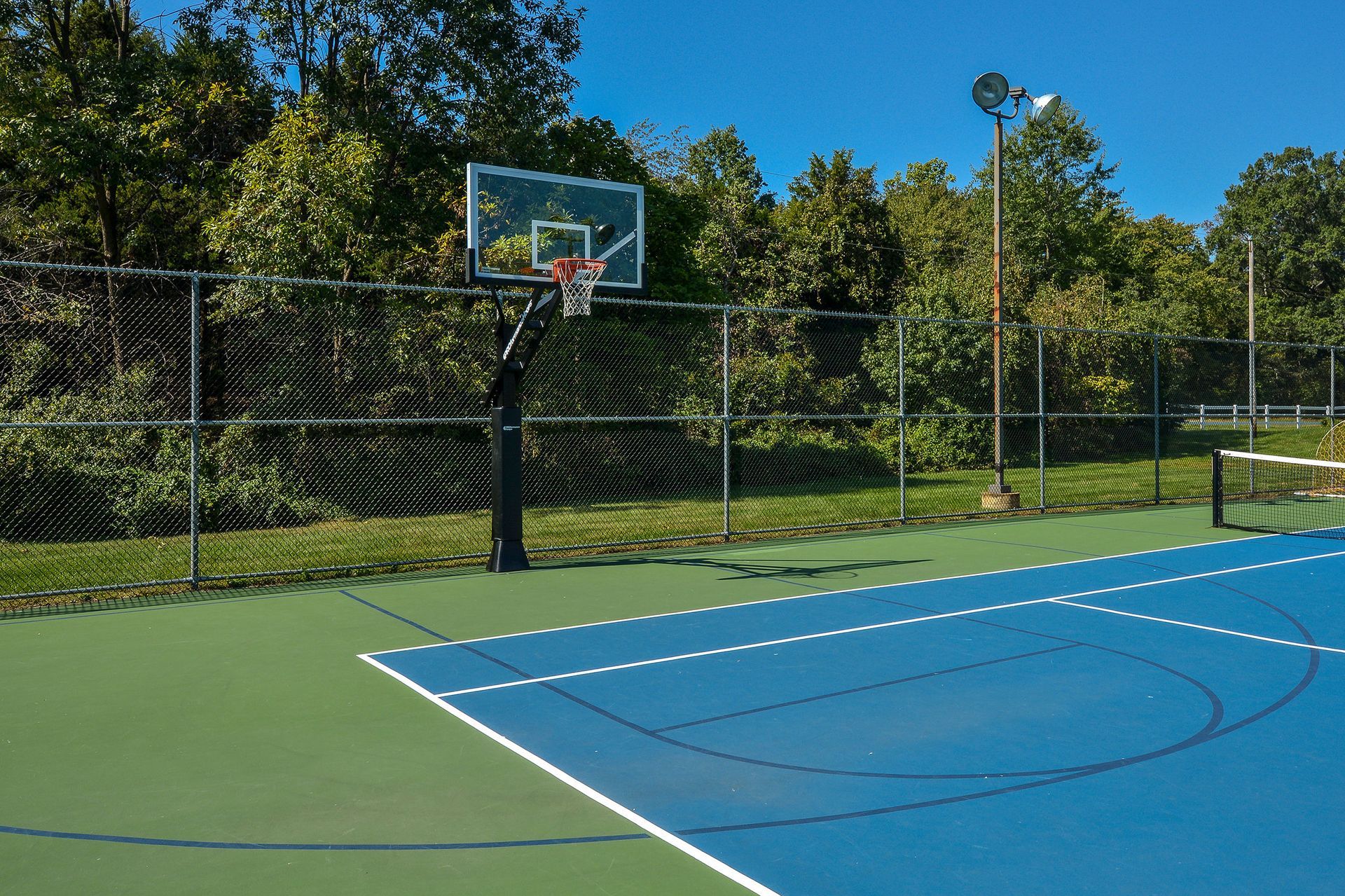 Outdoor basketball court with hoop, backboard, and chain-link fence.