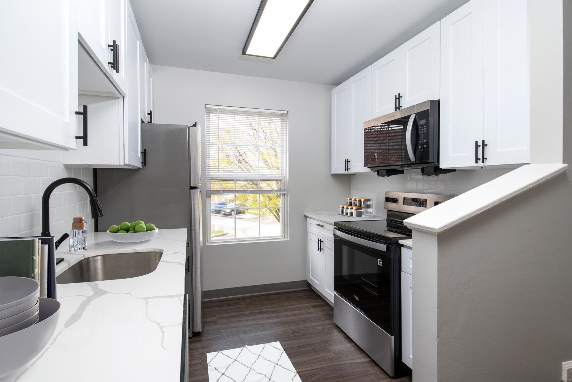 Bright galley kitchen with white cabinets, stainless steel appliances, and a window.