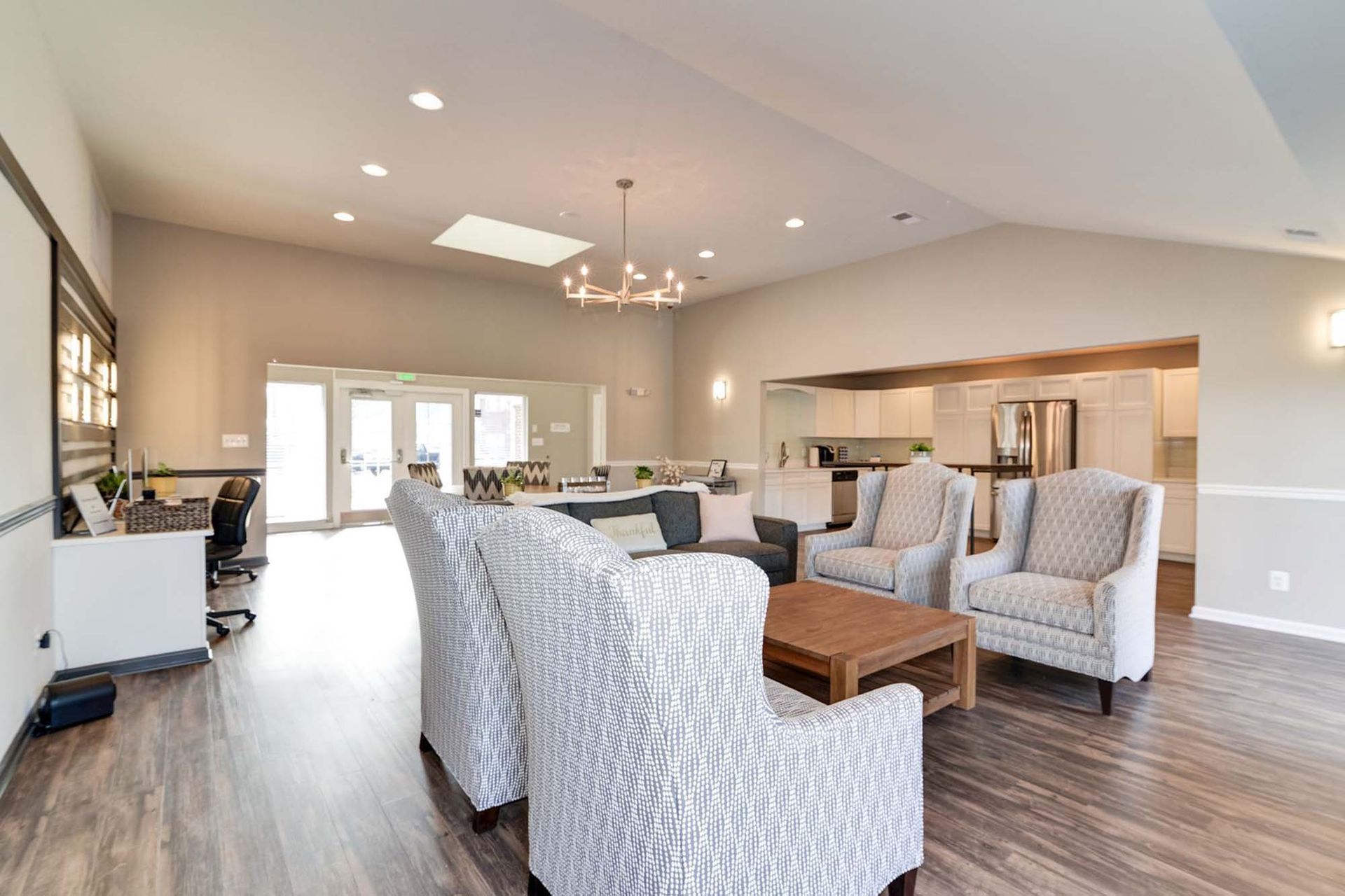 Bright community lounge with neutral seating and a kitchenette in the background.