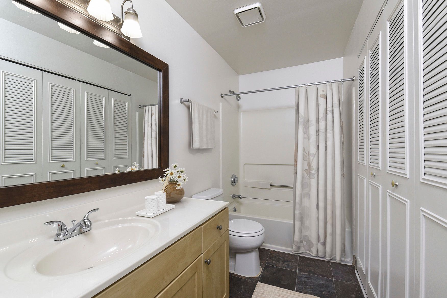 Bathroom with white vanity, wood-framed mirror, toilet, and tub/shower.