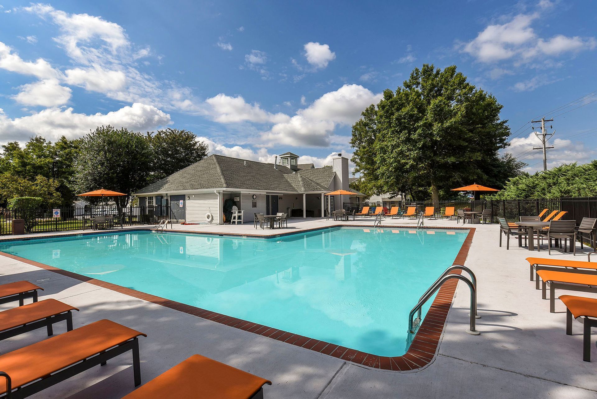 Outdoor swimming pool with orange lounge chairs and umbrellas at a gated apartment community.