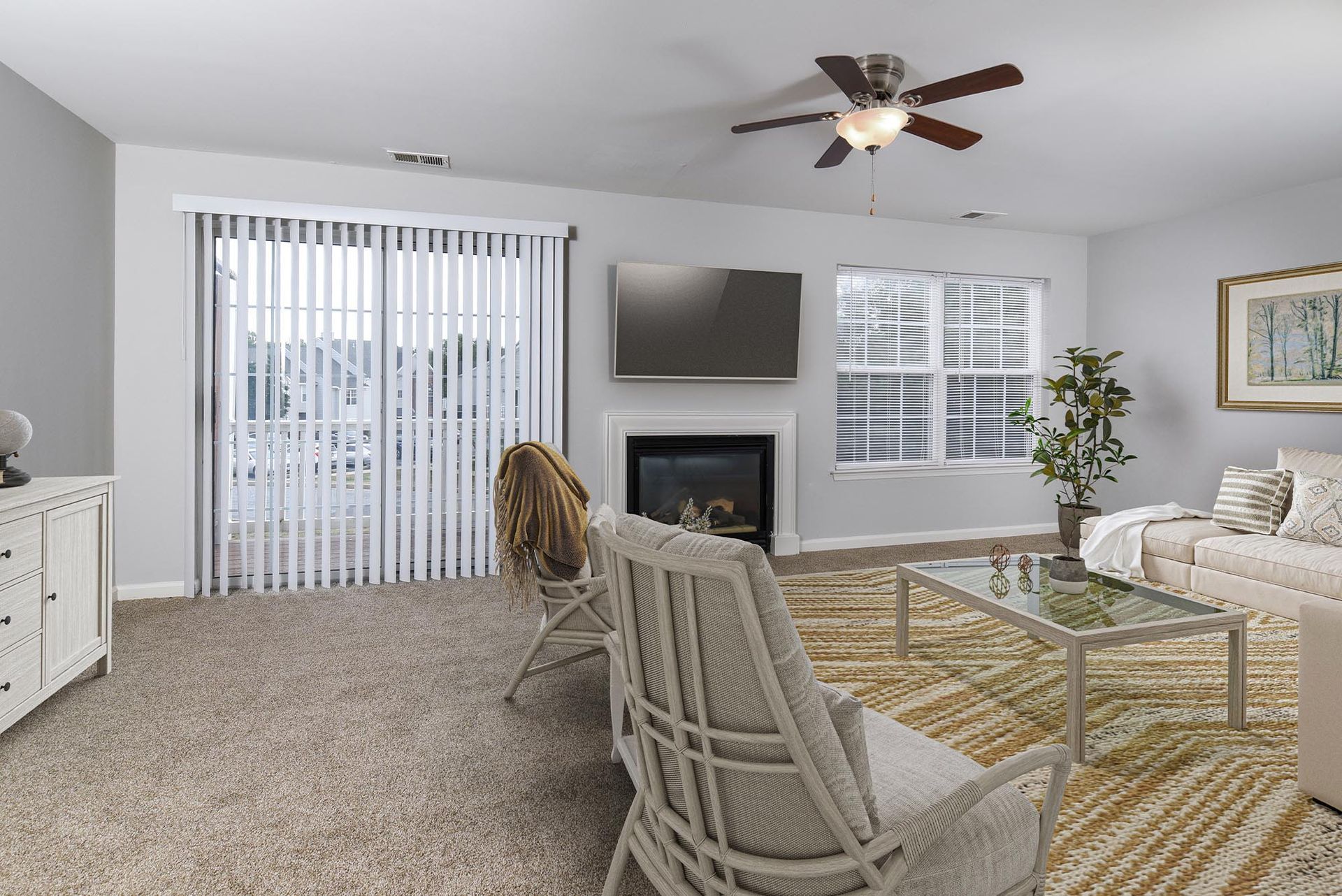 Living room in apartment with fireplace, wall TV, ceiling fan, beige furniture, and sliding door with vertical blinds.
