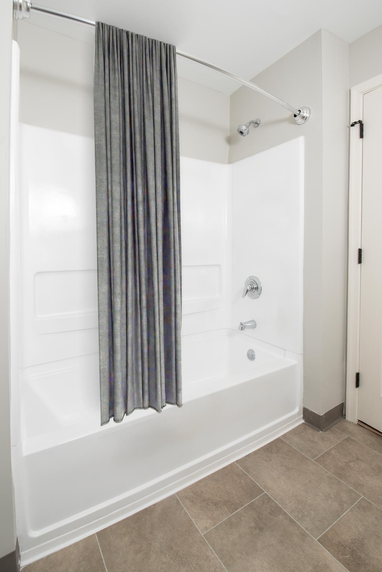 White bathtub with a gray shower curtain in a neutral-toned bathroom.
