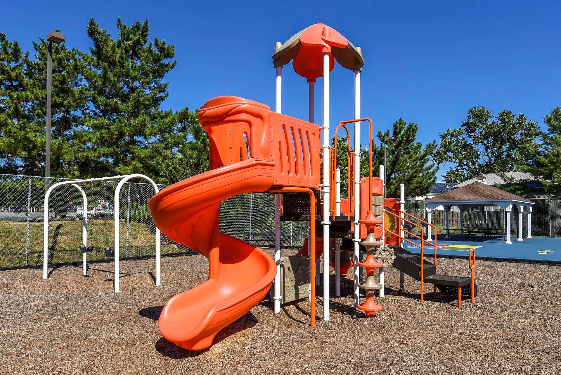Orange playground structure with a twisting slide in a fenced community park.