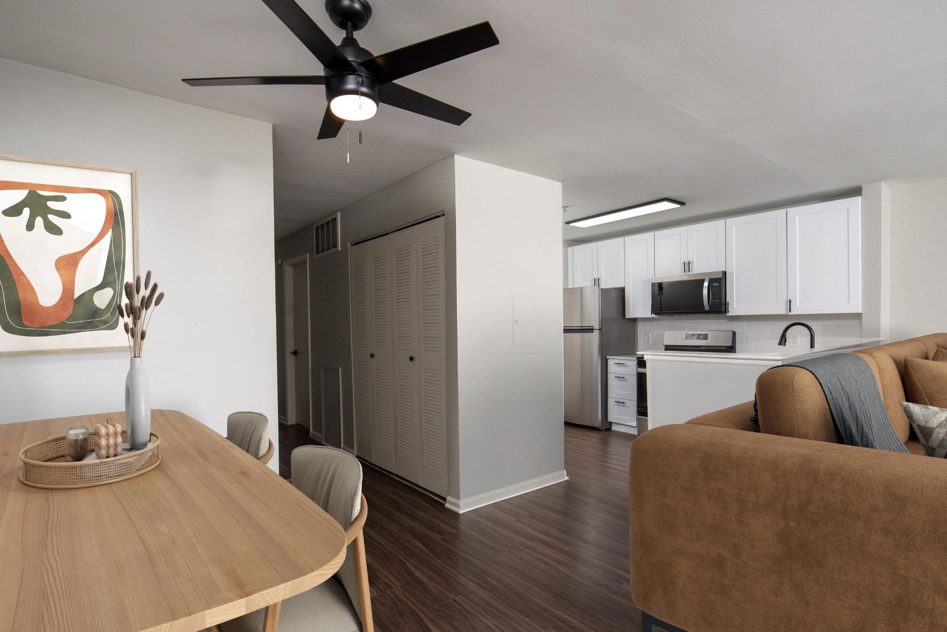 Open-concept living area with a dining table, white kitchen, and brown sofa.