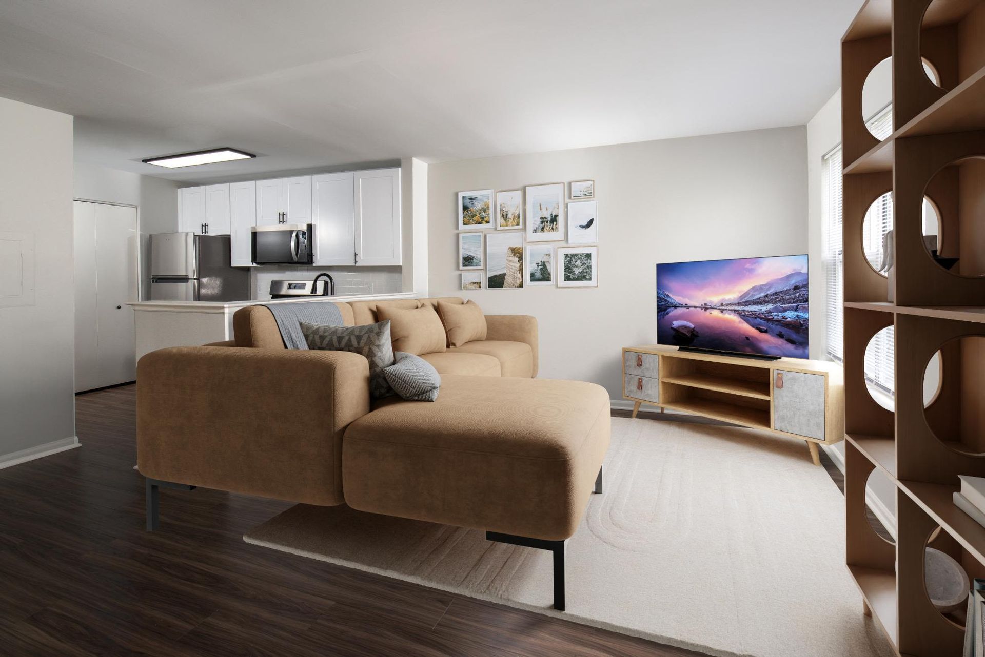 Living room with a tan sectional sofa, TV on a stand, and open kitchen in a modern apartment.