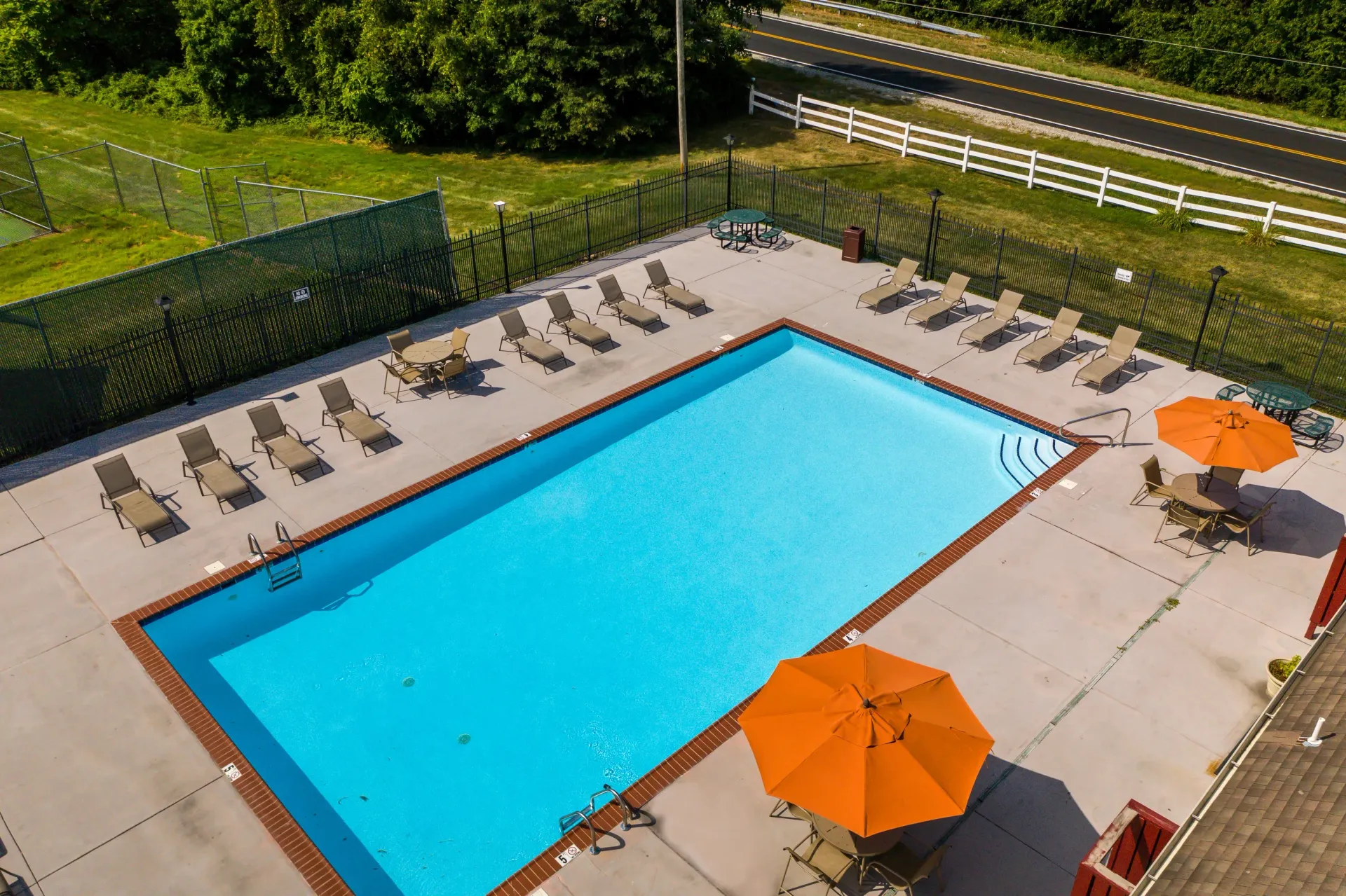 Aerial view of an outdoor rectangular pool surrounded by lounge chairs, tables, and orange umbrellas.