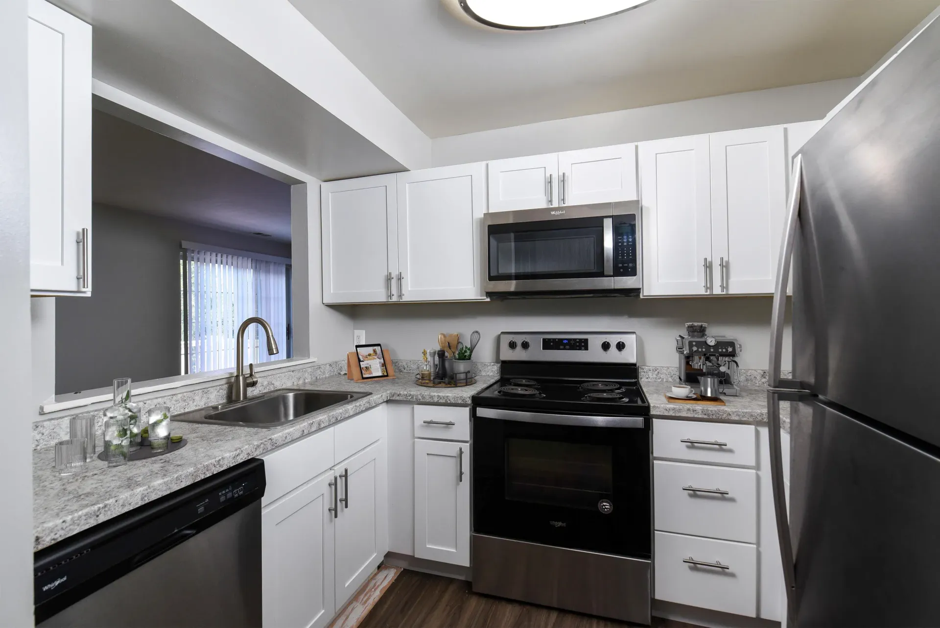 White kitchen with granite countertops, stainless-steel appliances, and a pass-through window.