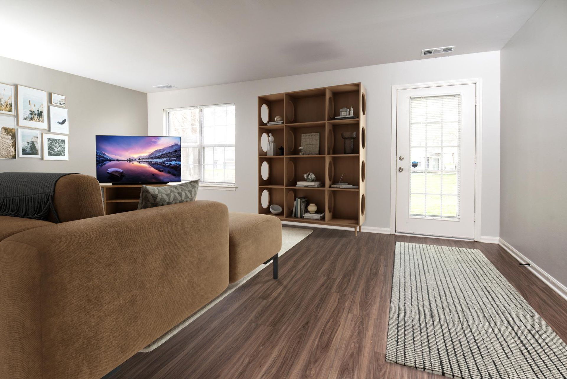 Living room in an apartment with a brown sectional sofa, TV, and a tall bookshelf near a glass door.