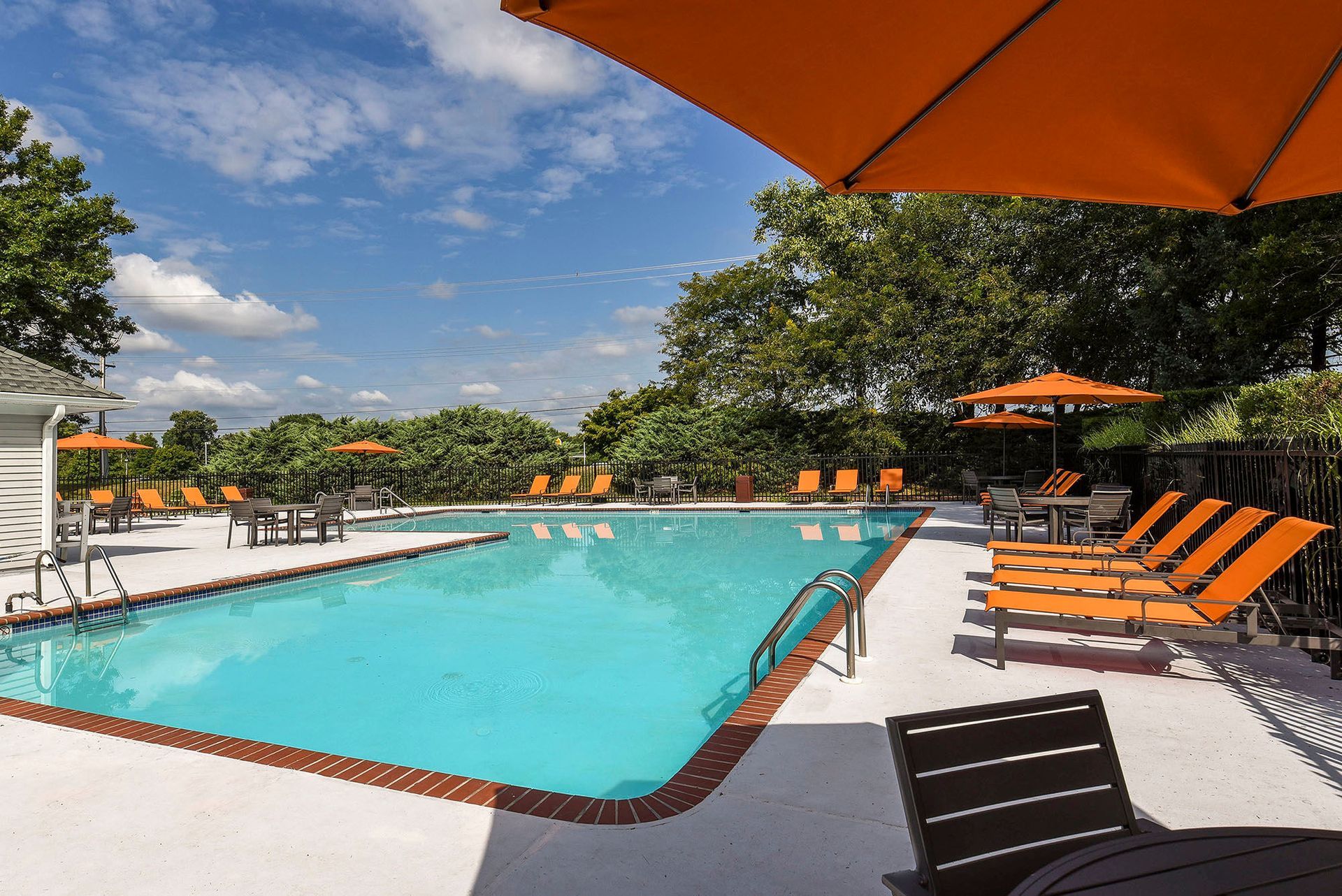 Outdoor community pool area with orange lounge chairs and umbrellas.