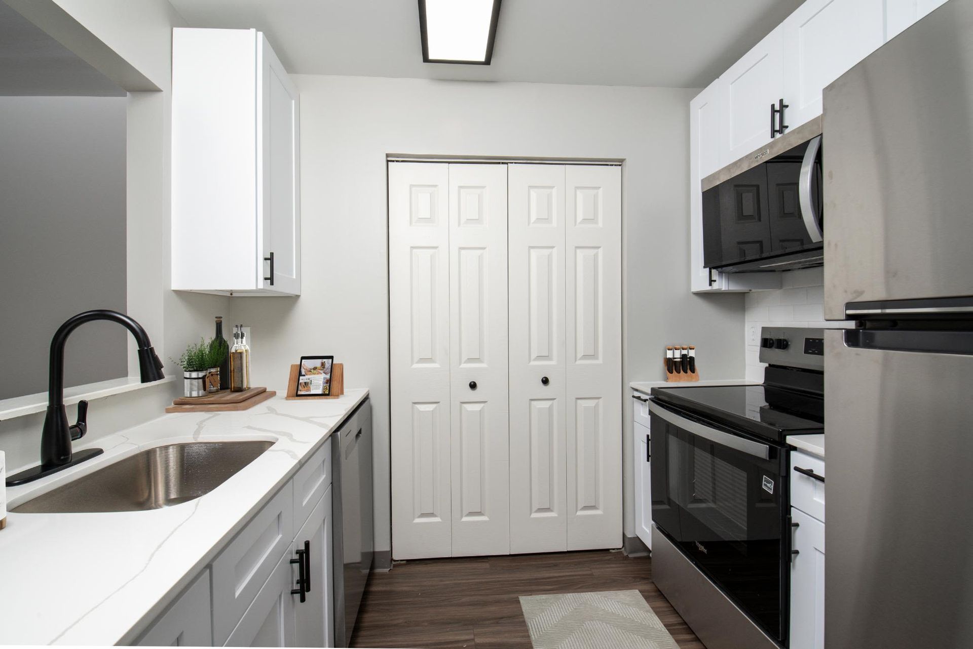Modern apartment kitchen with white cabinets, quartz countertops, and stainless steel appliances.