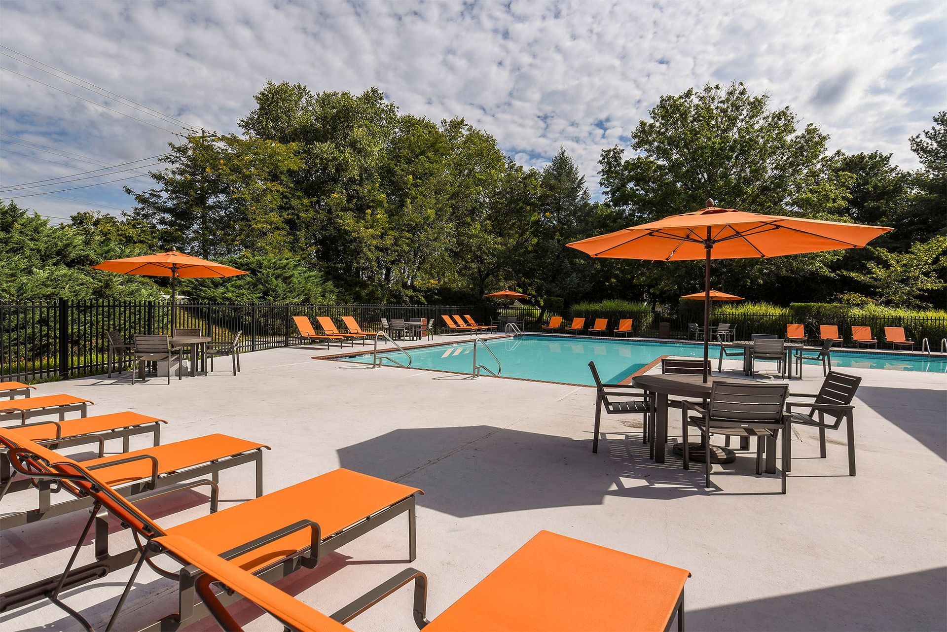 Outdoor pool deck with orange lounge chairs and umbrellas.