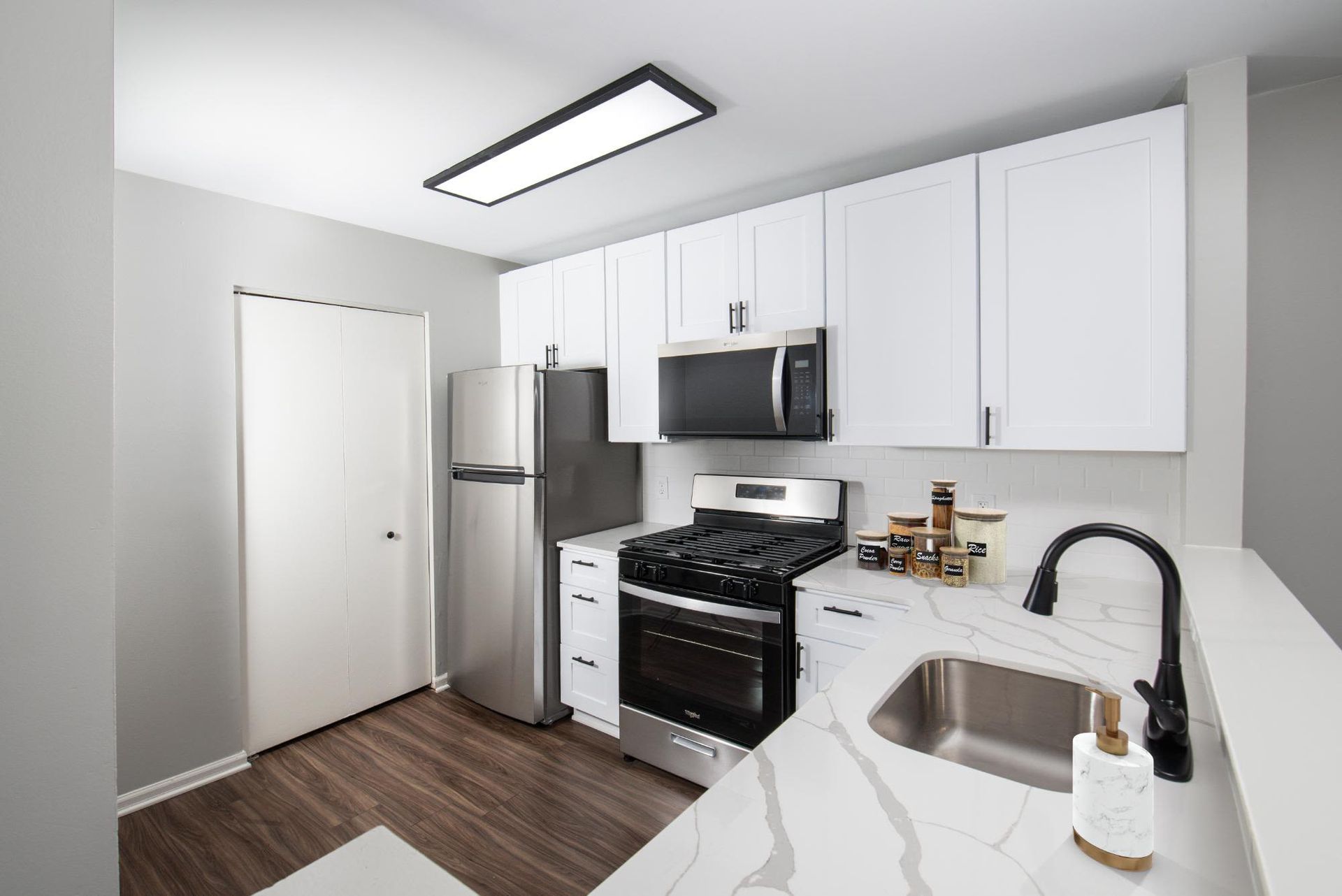 Modern white kitchen with stainless steel appliances and marble-pattern countertops.
