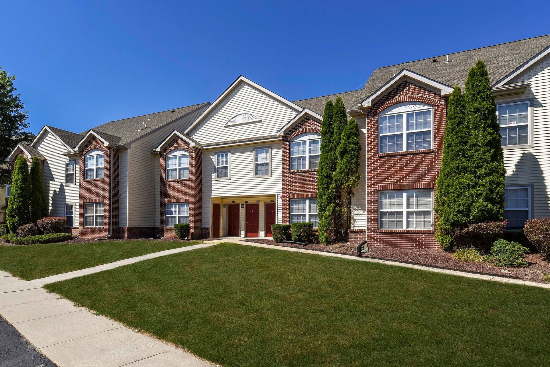 Exterior view of a multi-unit apartment building with brick accents and manicured lawn.