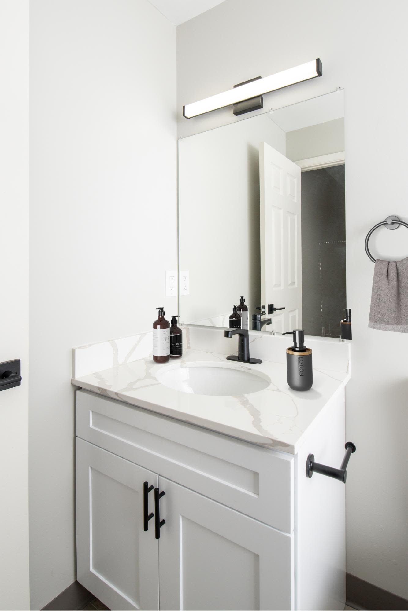 Bathroom vanity with white cabinet, marble countertop, and a large mirror.