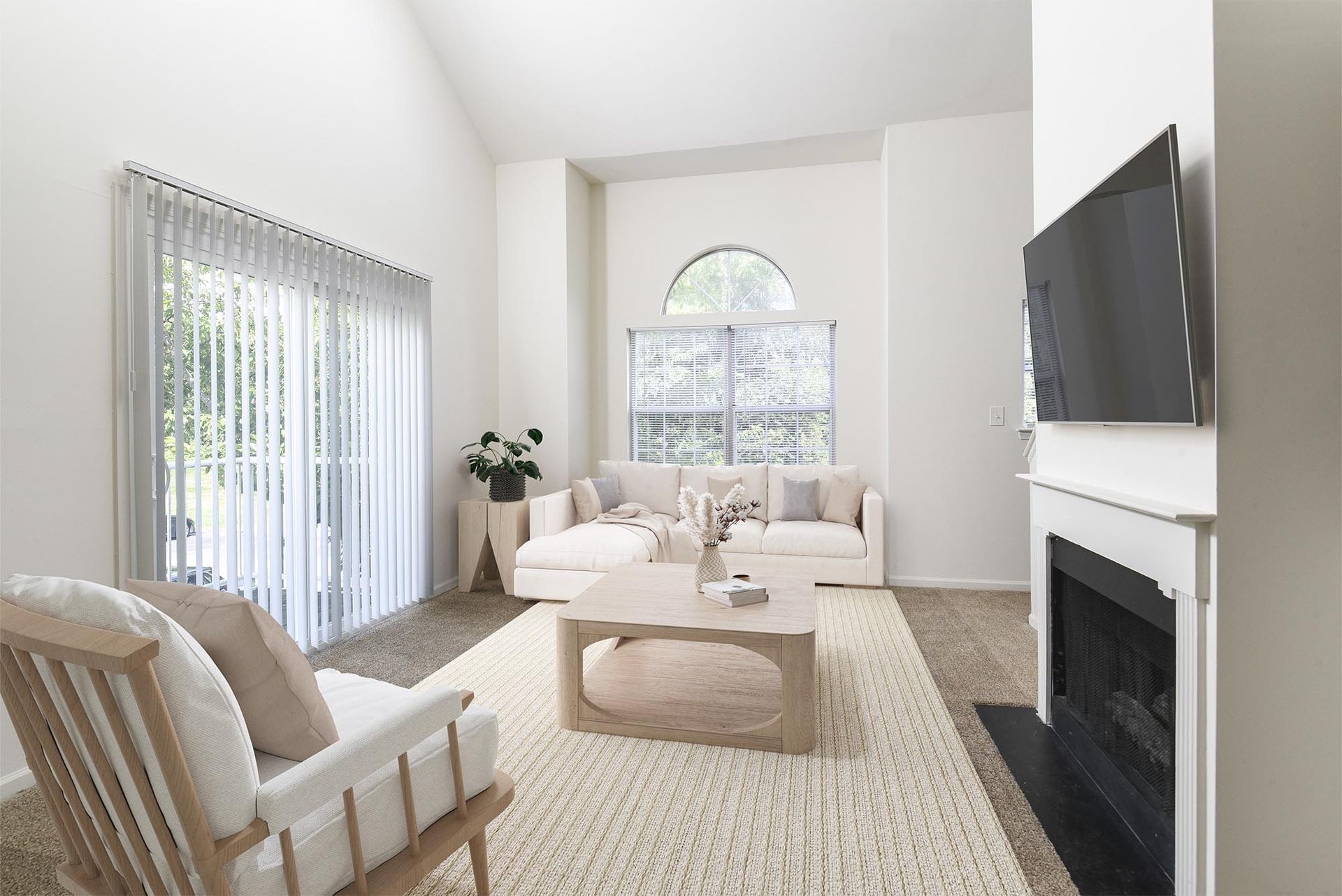 Bright living room with a beige sofa, armchair, fireplace, and large windows with blinds.
