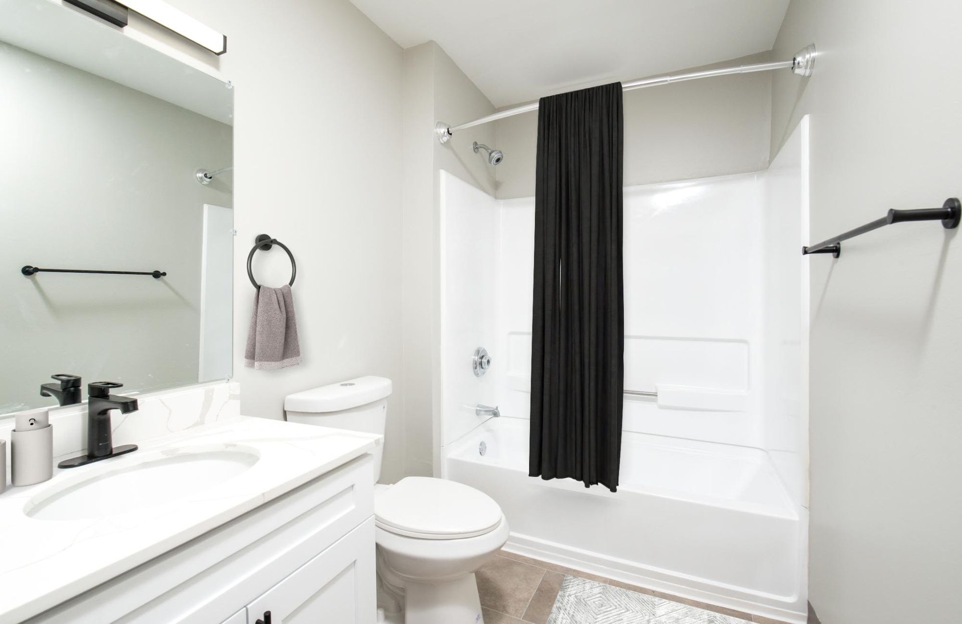 Soothing, modern bathroom with white vanity, toilet, and a bathtub/shower with a black curtain.