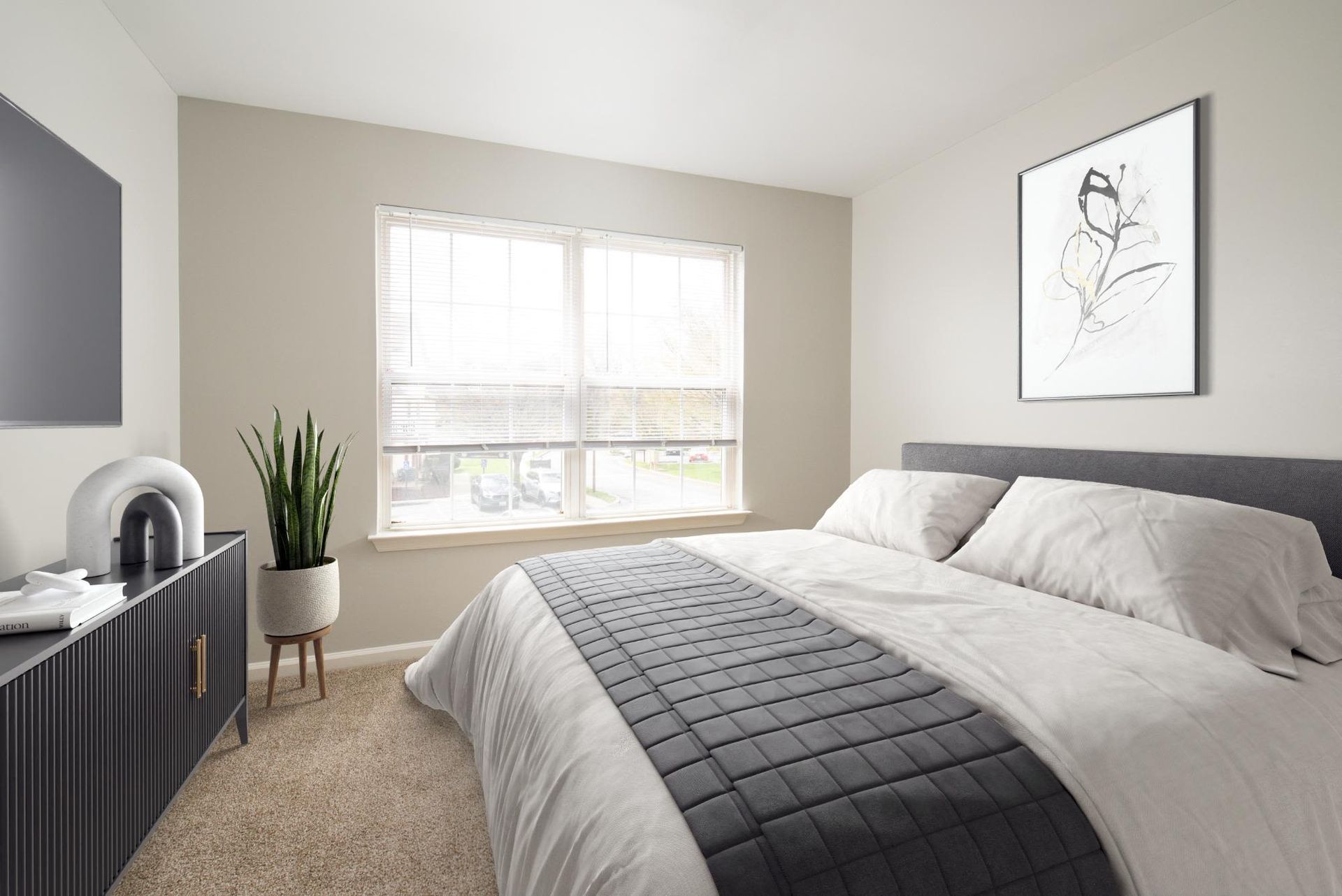 Bedroom in a modern apartment with a large window, bed, dresser, and plant.