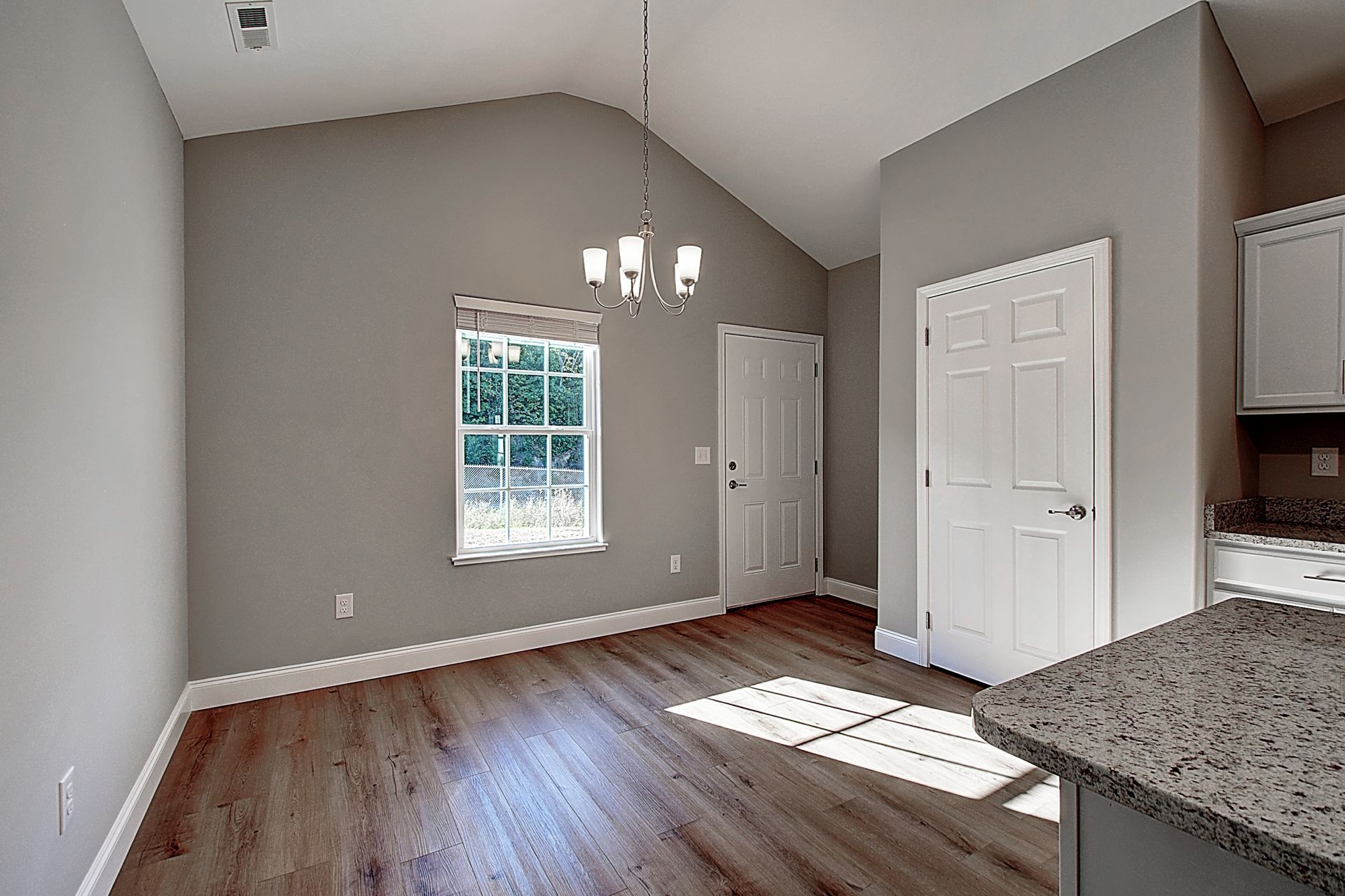 An empty living room with hardwood floors and a vaulted ceiling.
