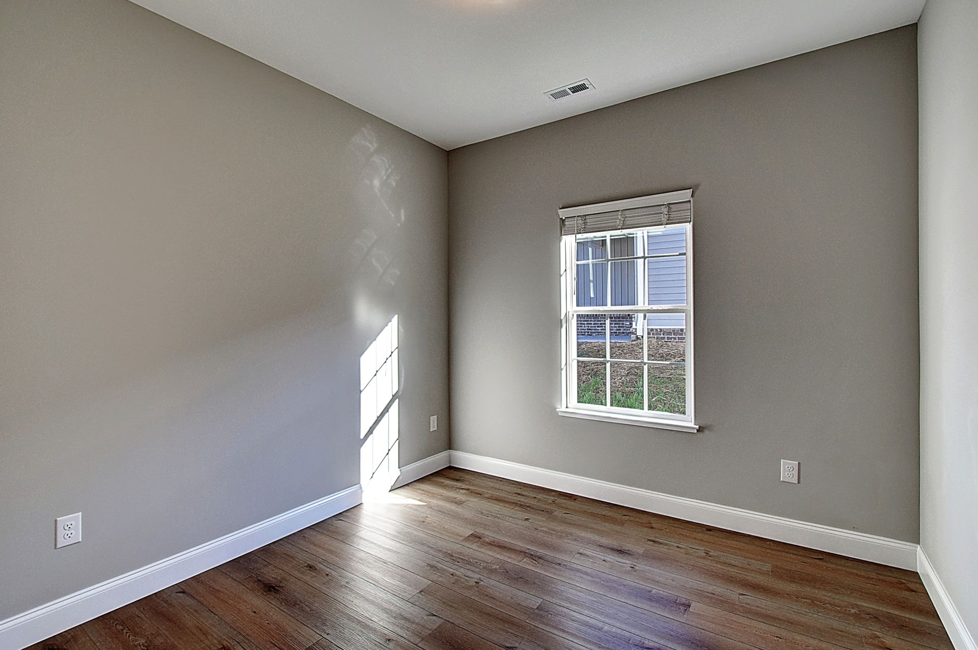 An empty room with a window and hardwood floors.