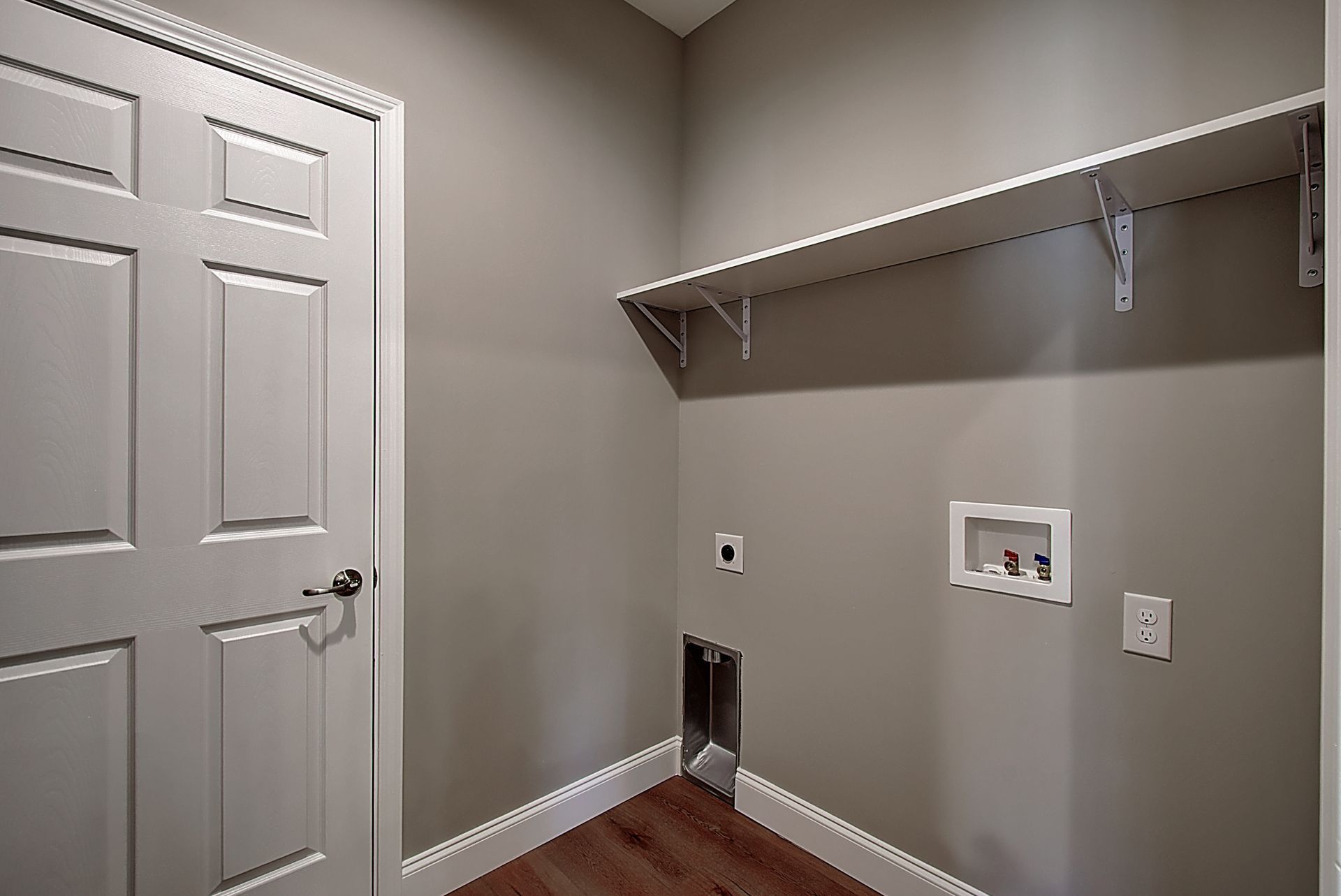 A laundry room in a house with a door and a shelf.