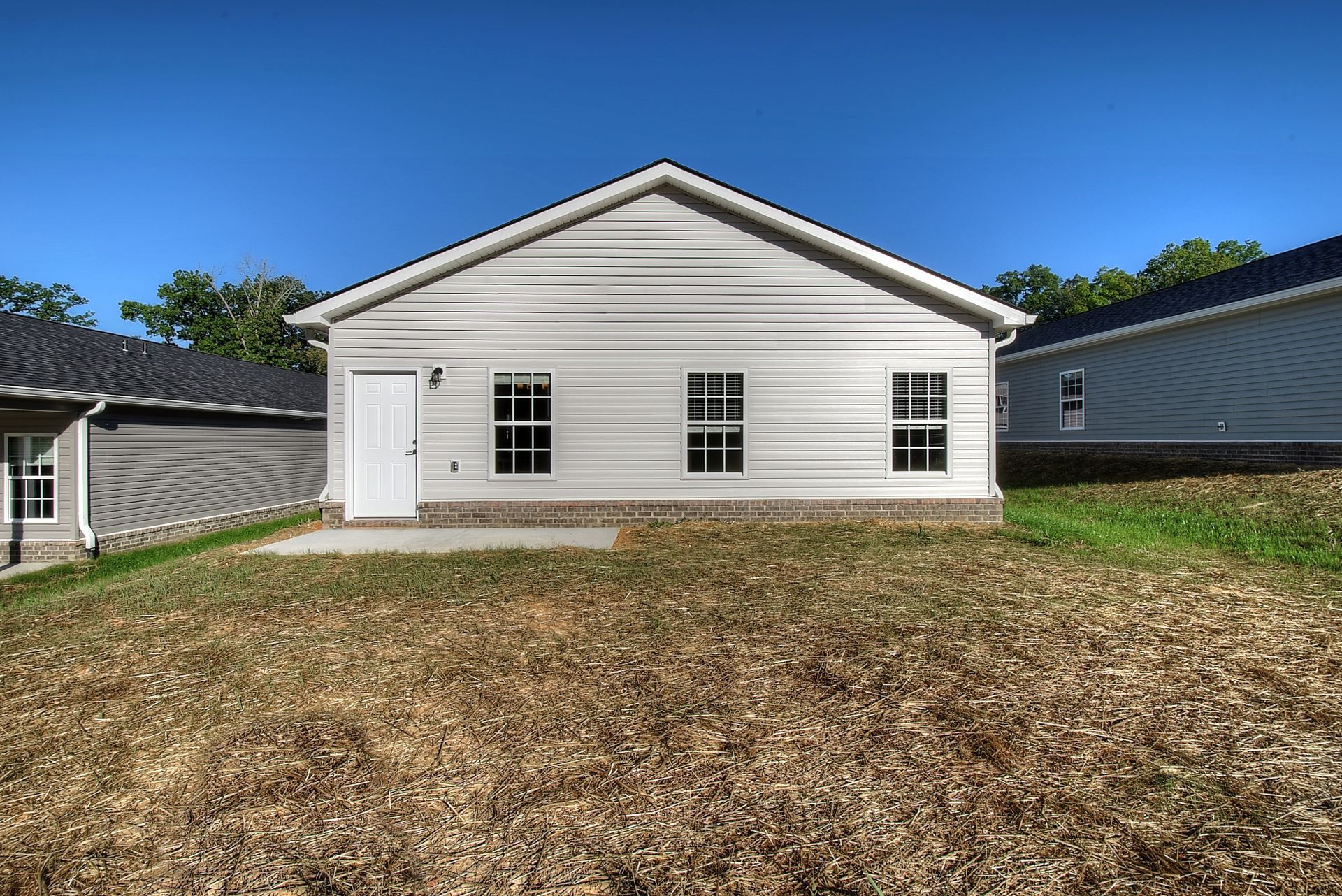 A white house with a lot of windows is sitting on top of a grassy hill.