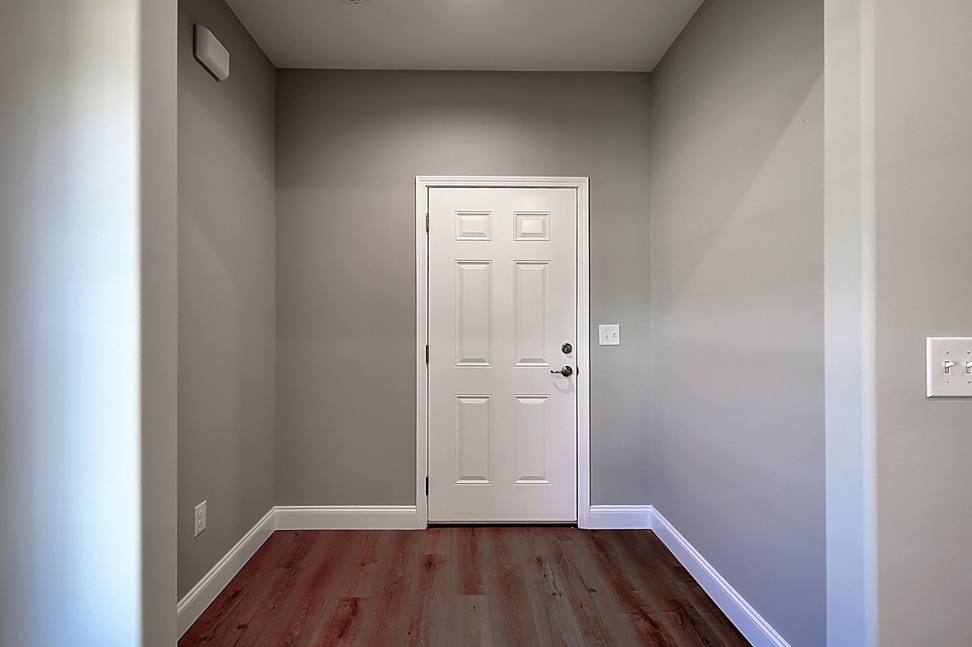 An empty hallway with a white door and hardwood floors.