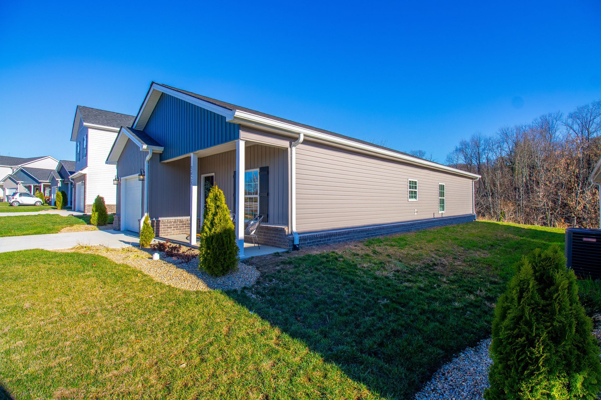 A house with a porch and a garage is sitting on top of a lush green field.