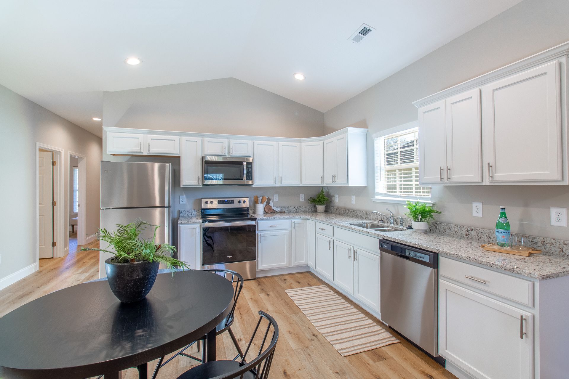 A kitchen with white cabinets , stainless steel appliances , a table and chairs.