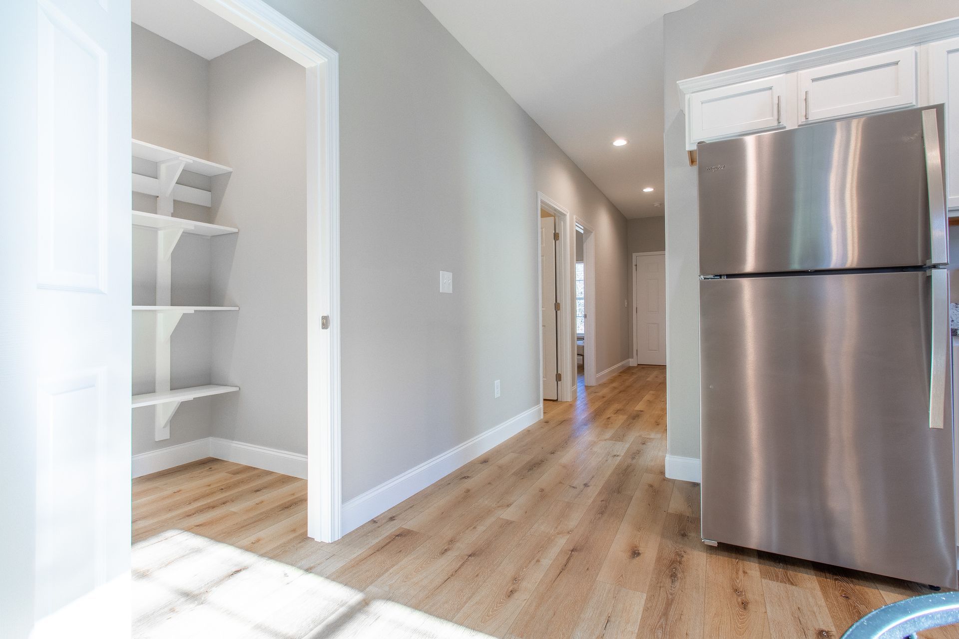 A stainless steel refrigerator is sitting in a hallway next to a pantry.