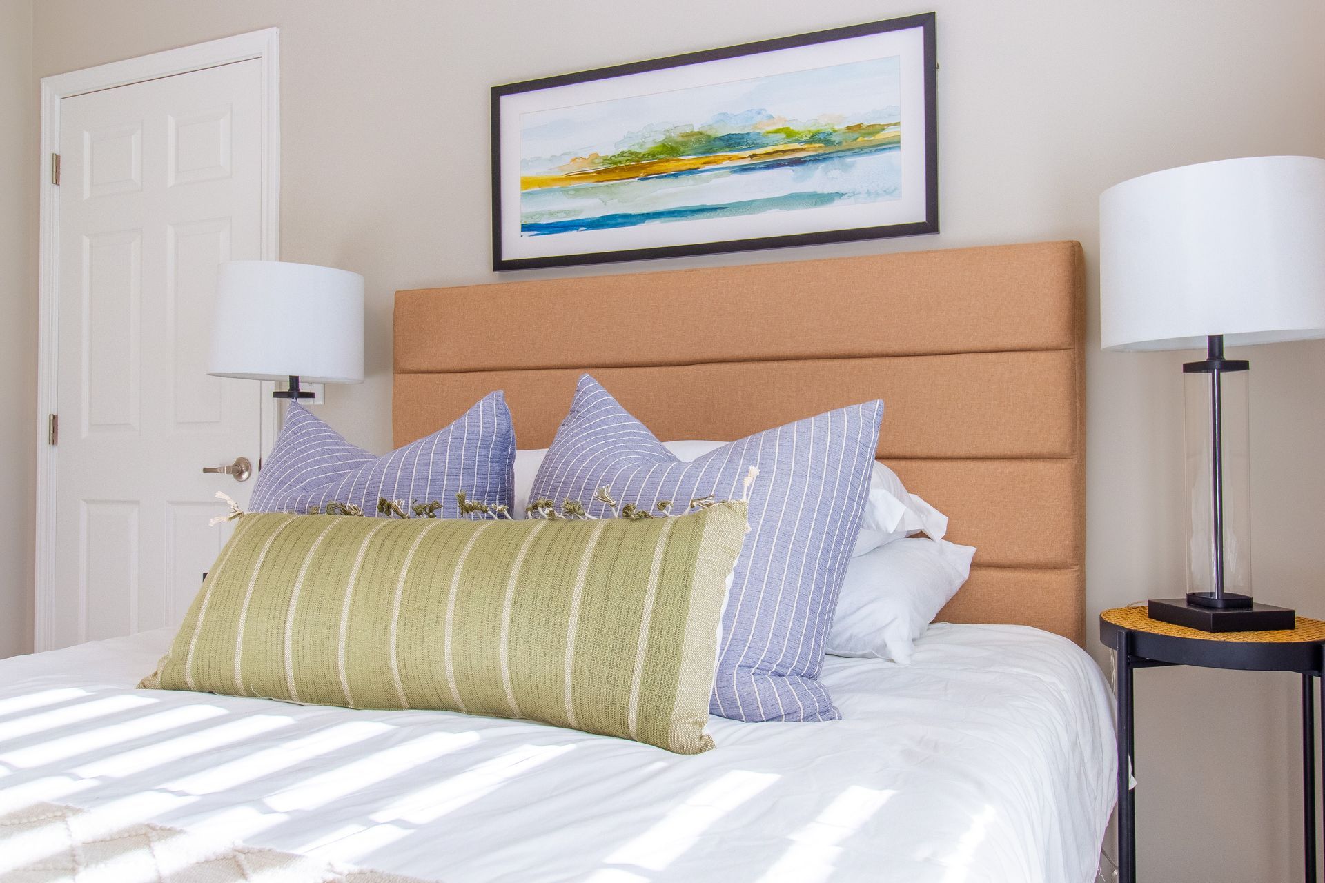 A bedroom with a bed , two lamps and a painting on the wall.