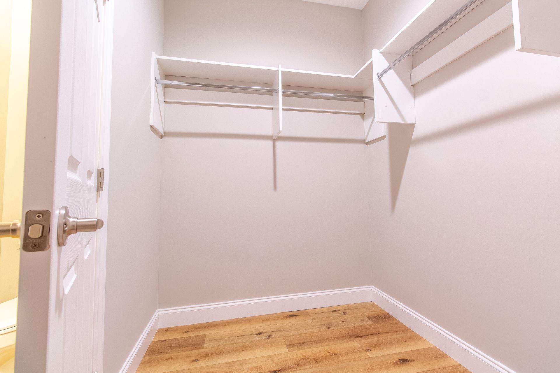 An empty walk in closet with hardwood floors and white shelves.
