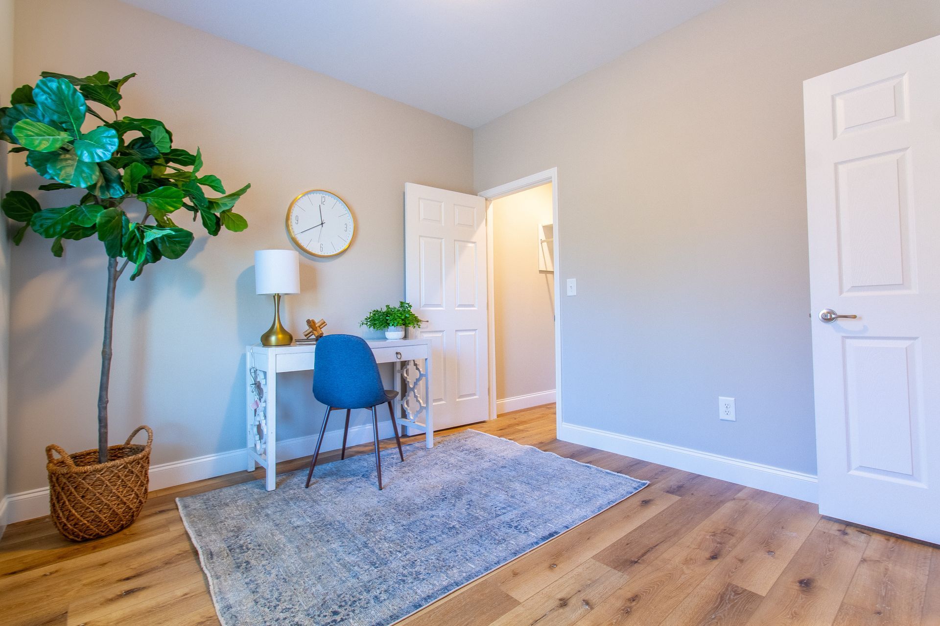 A room with a desk , chair , plant and a clock on the wall.