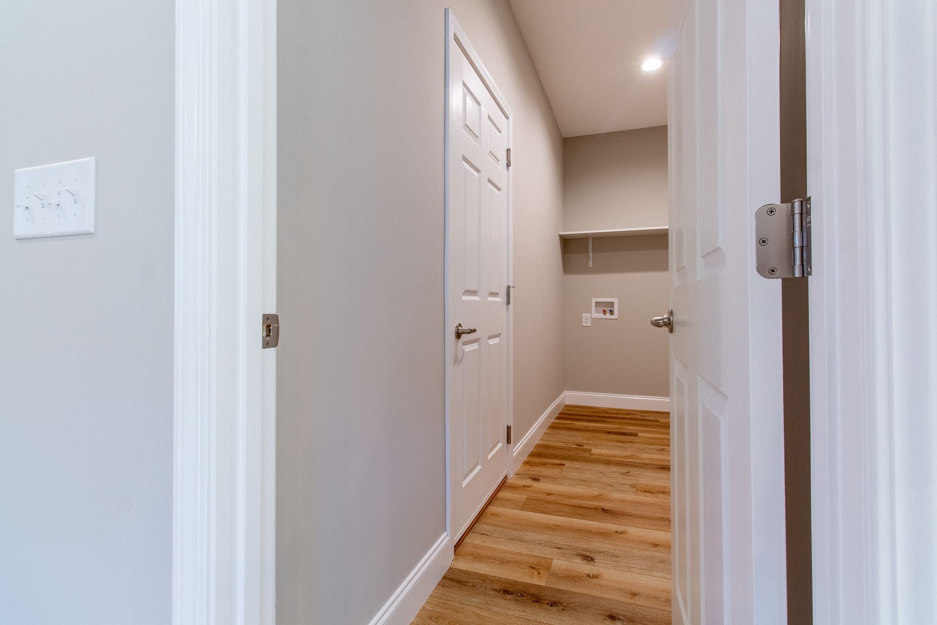 A hallway with a wooden floor and a white door leading to a laundry room.