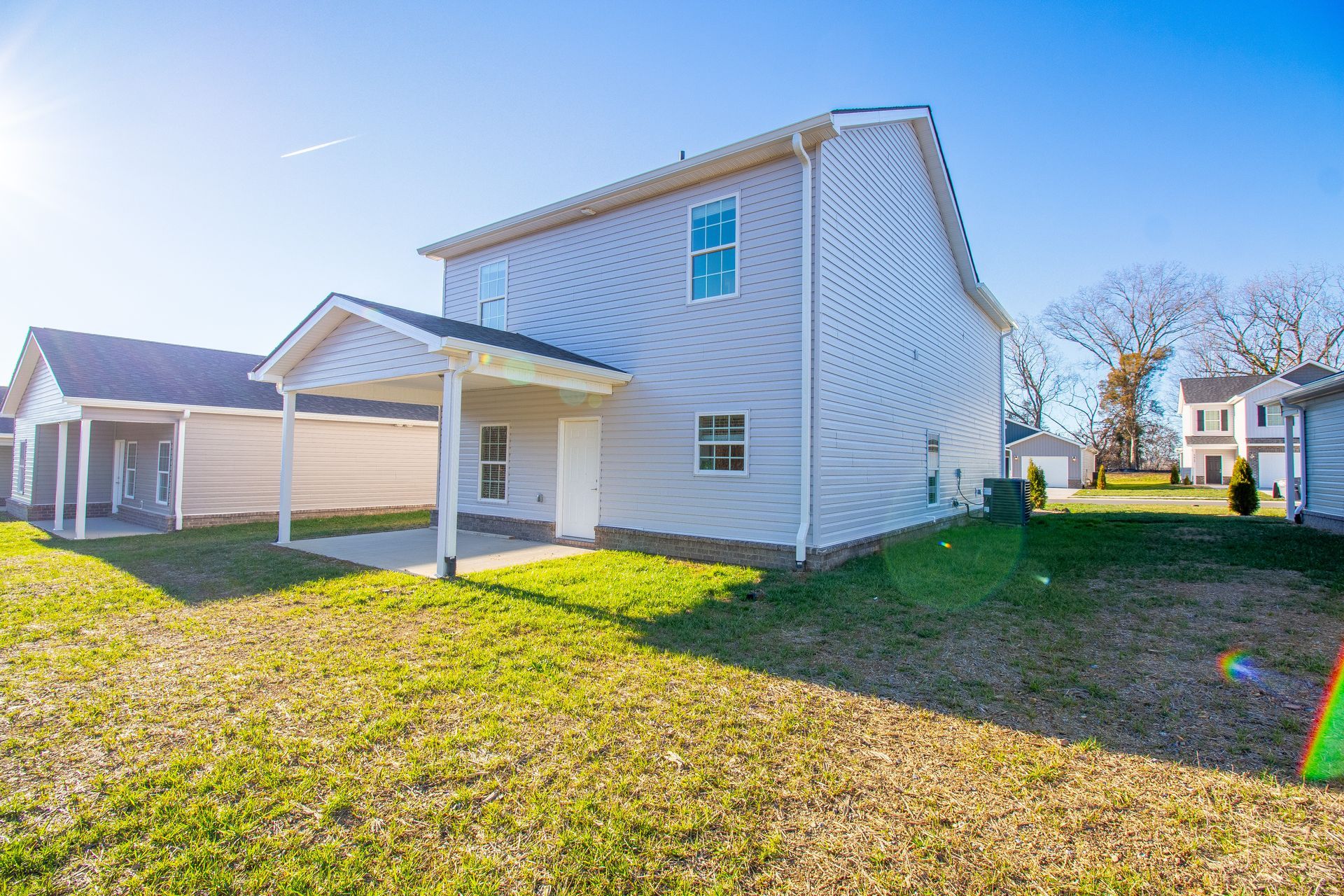 A large white house with a covered porch is sitting on top of a lush green field.