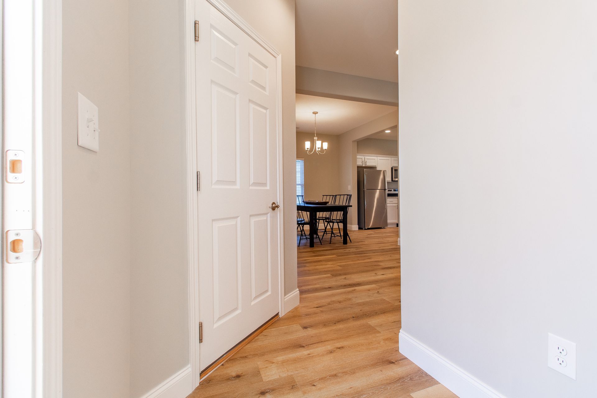 A hallway in a house with hardwood floors and a white door leading to a dining room.