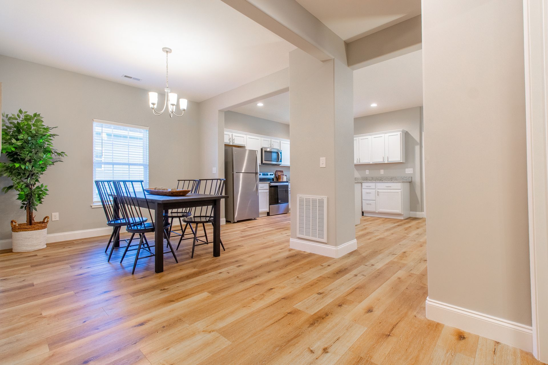 A dining room with a table and chairs and a kitchen in the background.