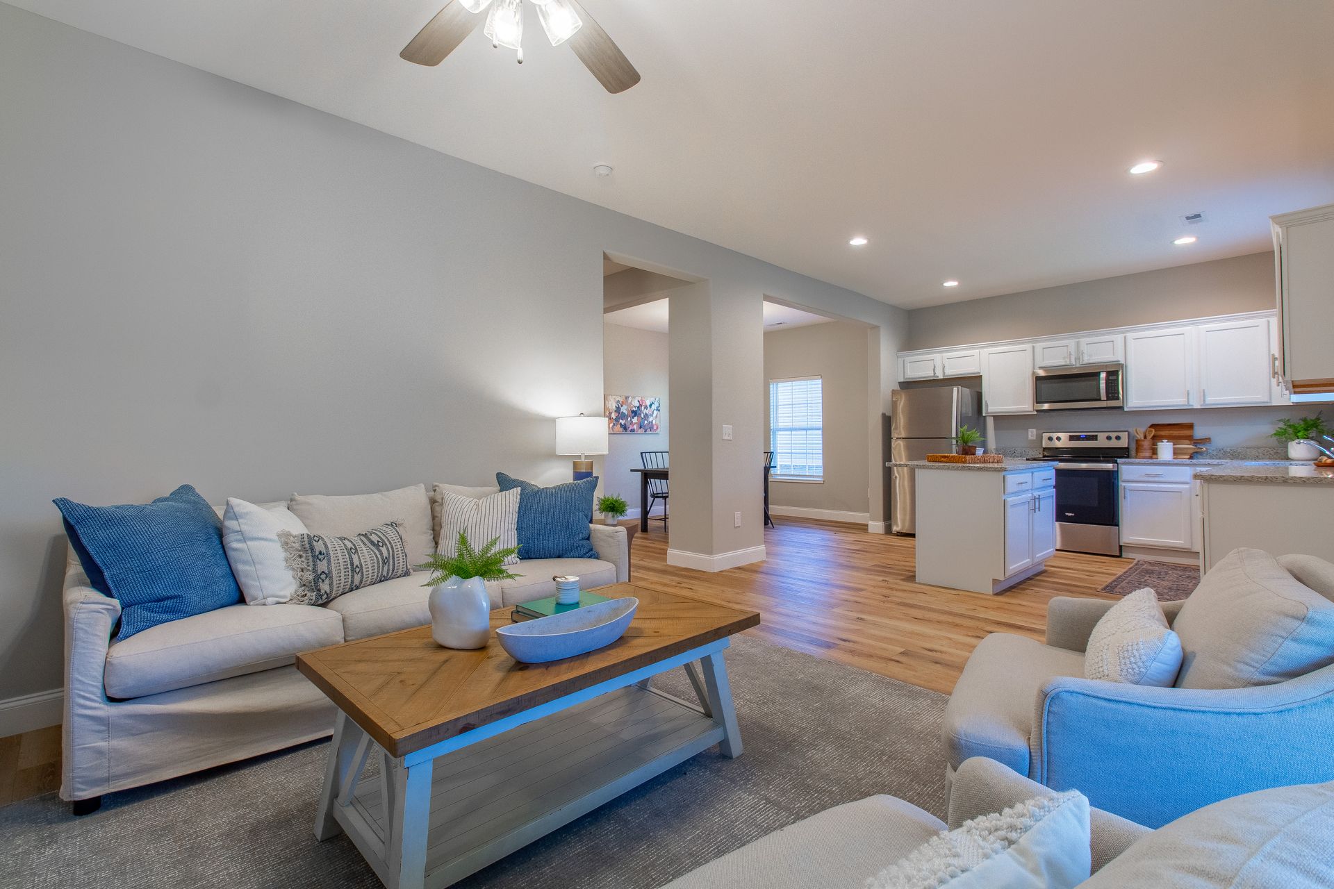 A living room with a couch , chair , coffee table and ceiling fan.