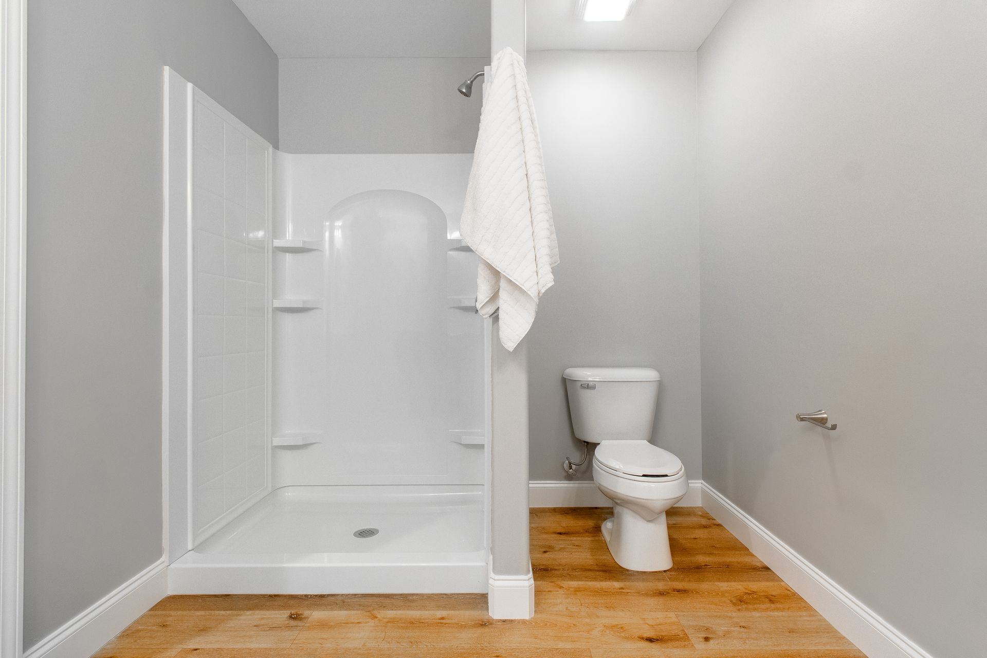 A bathroom with a toilet , shower and wooden floor.