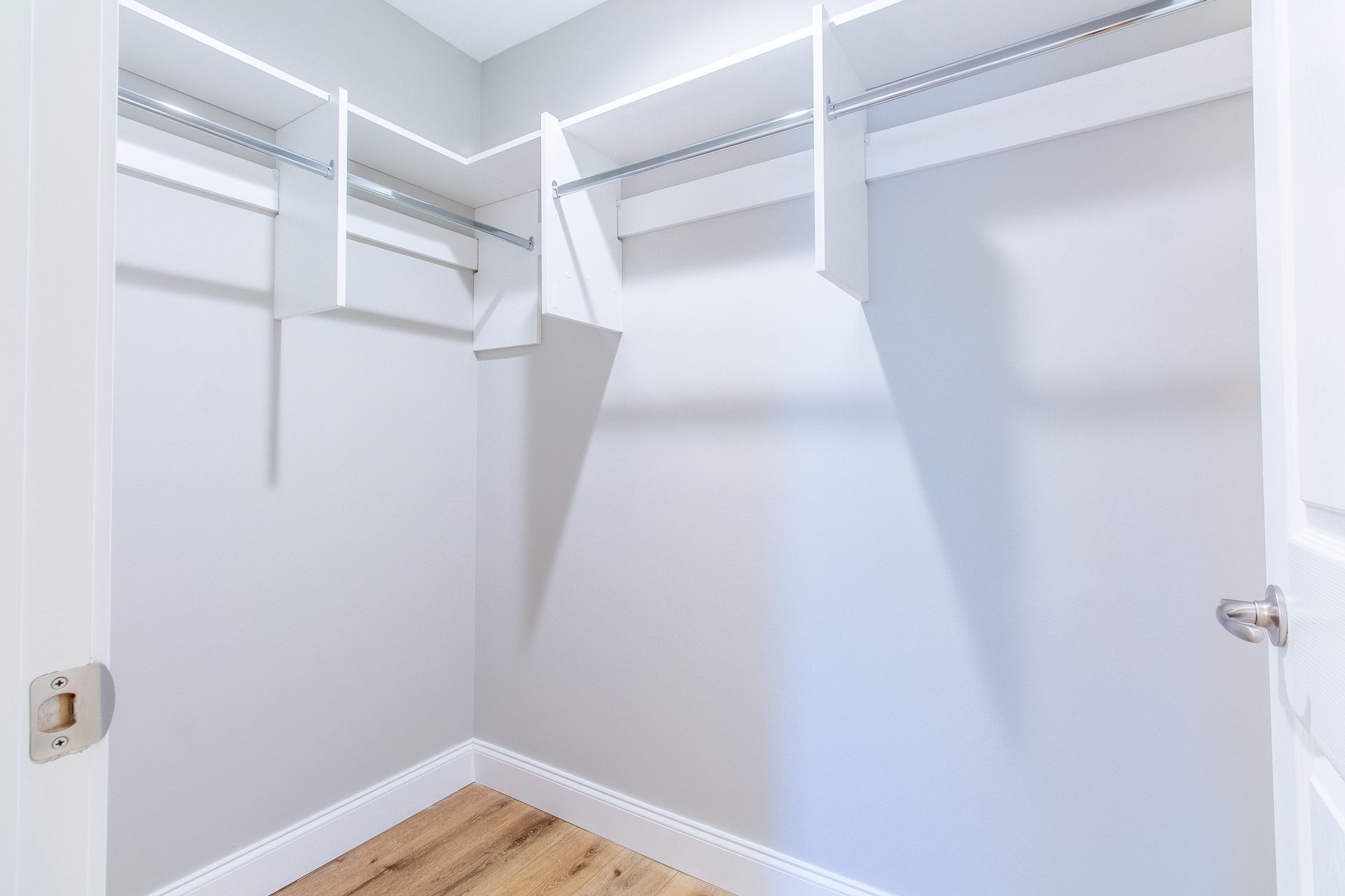 An empty walk in closet with hardwood floors and white shelves.