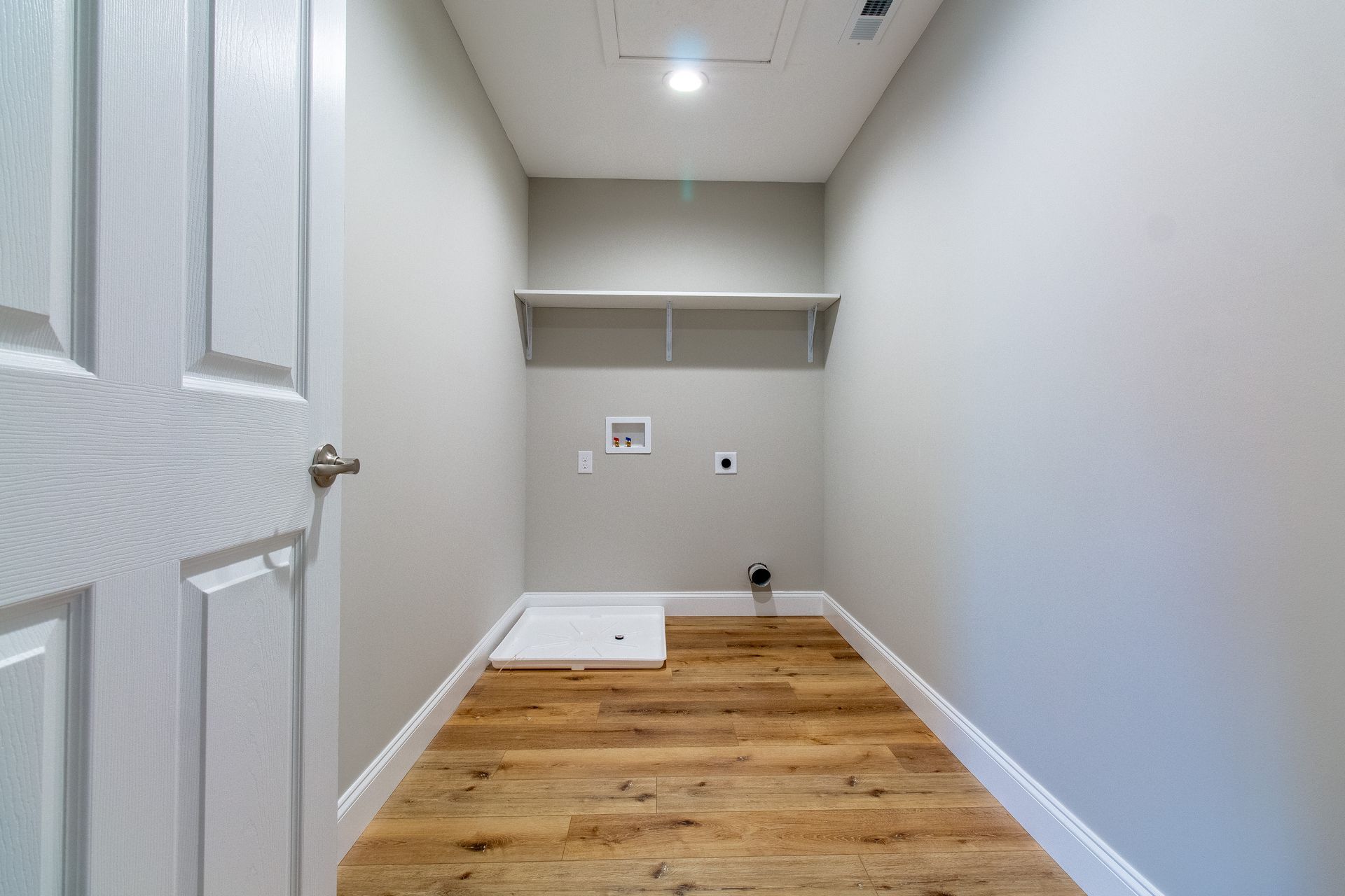 An empty laundry room with hardwood floors and a door.