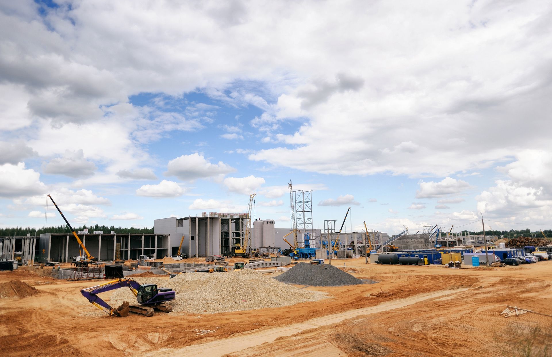 Construction site with cranes, earthmovers, and partially built buildings under a cloudy sky.