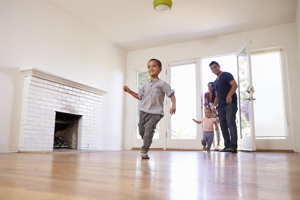 A Family Is Standing In An Empty Living Room In Their New Home — Brisbane Moving & Storage In Acacia Ridge, QLD