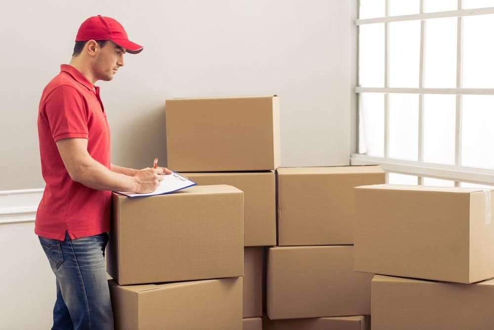 A Delivery Man Is Standing Next To A Pile Of Cardboard Boxes — Brisbane Moving & Storage In Acacia Ridge, QLD