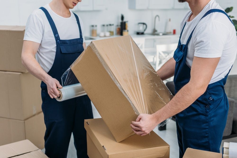 Two Men Are Wrapping A Cardboard Box With Plastic Wrap — Brisbane Moving & Storage In Acacia Ridge, 